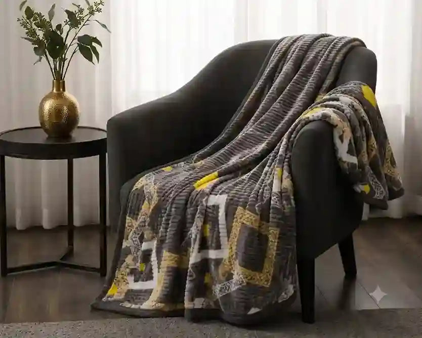 A textured throw blanket with a gray, yellow, and white geometric pattern draped over a dark gray armchair in a living room setting next to a side table with a gold vase.