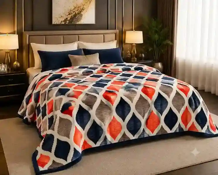 A bed dressed in a patterned quilted blanket featuring a geometric diamond lattice in navy blue, orange, gray, and white, styled in a modern bedroom setting.