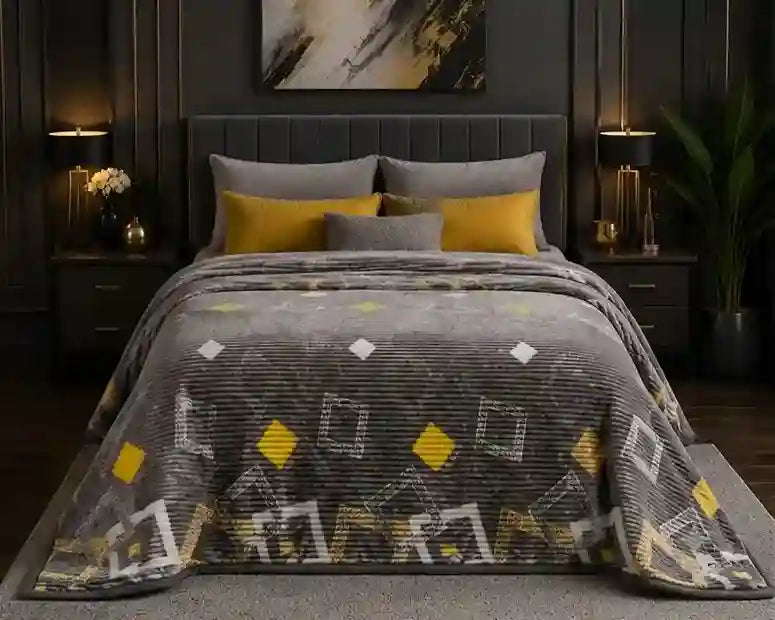 A gray textured blanket with yellow and white geometric diamond and square patterns is styled on a bed in a modern, dark-themed bedroom setting.