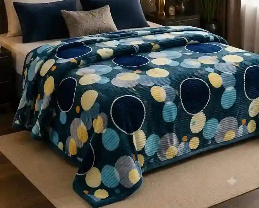 A plush blanket with a bold circular dot pattern in navy, light blue, yellow, and gray, styled on a bed in a bedroom setting.