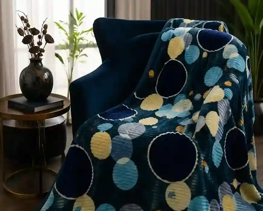 A dark blue throw blanket with a large circular dot pattern in navy, light blue, and yellow, draped over a dark blue armchair in a living room setting.