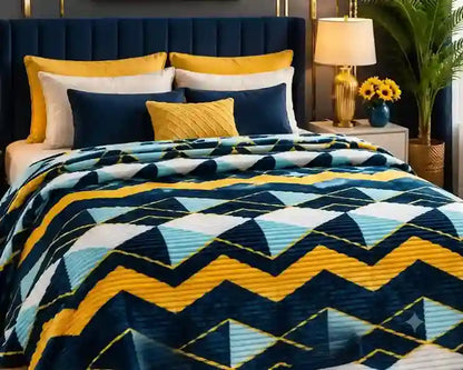 A bed dressed in a geometric patterned quilt with navy, yellow, and light blue zigzag and triangle motifs, styled with matching pillows in a modern bedroom setting.