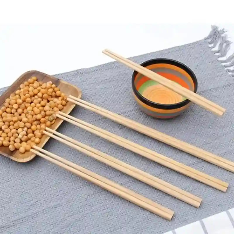 Five light natural wood chopsticks displayed on a gray textured cloth, with two resting in a small striped bowl and one pair placed in a shallow dish of round beige snacks.
