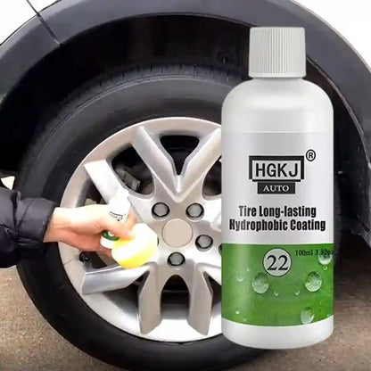 A bottle of HGKJ Auto Tire Long-lasting Hydrophobic Coating stands next to a car wheel, with a hand holding a yellow sponge touching the tire tread in a real outdoor setting.