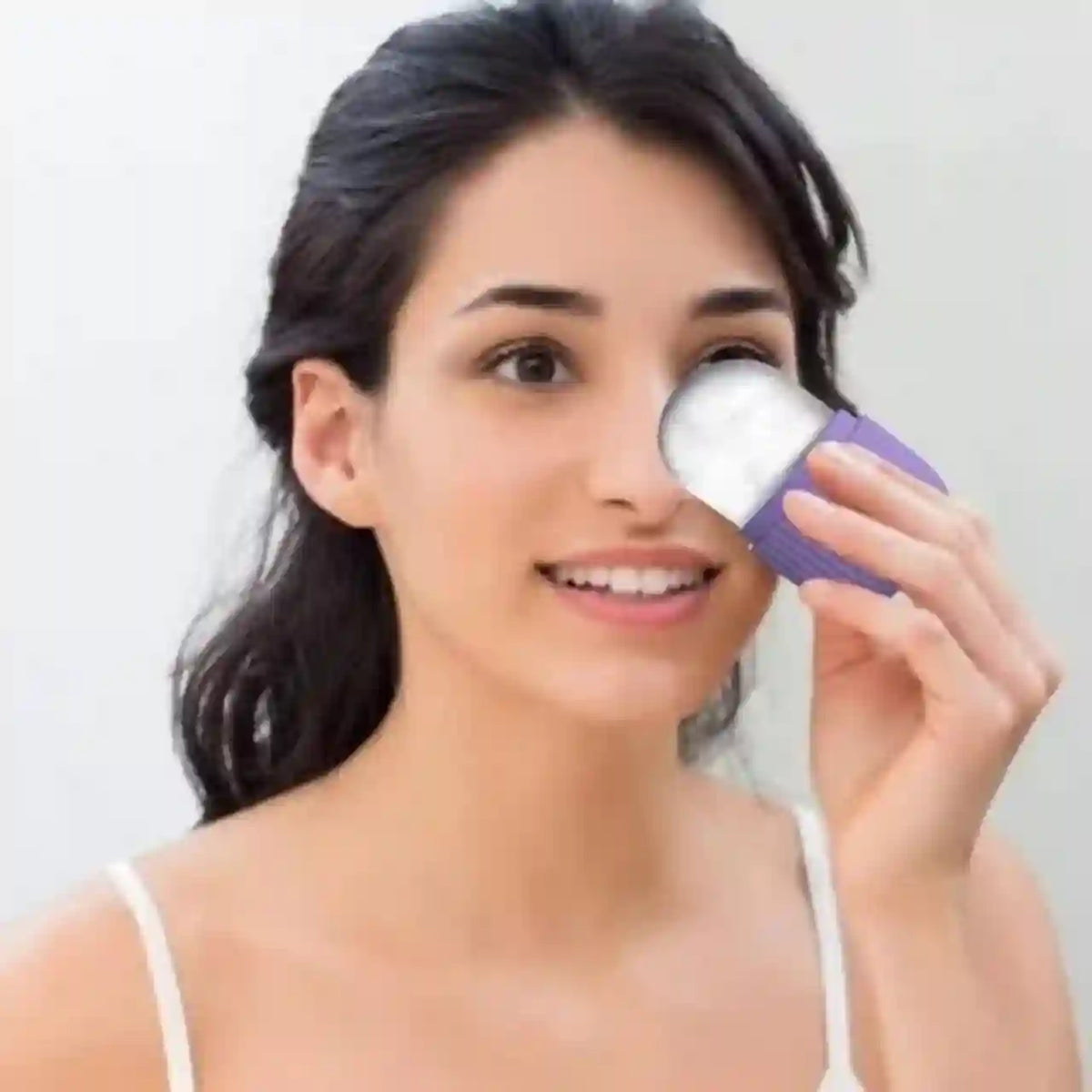 Woman using a skincare device on her face against a plain background