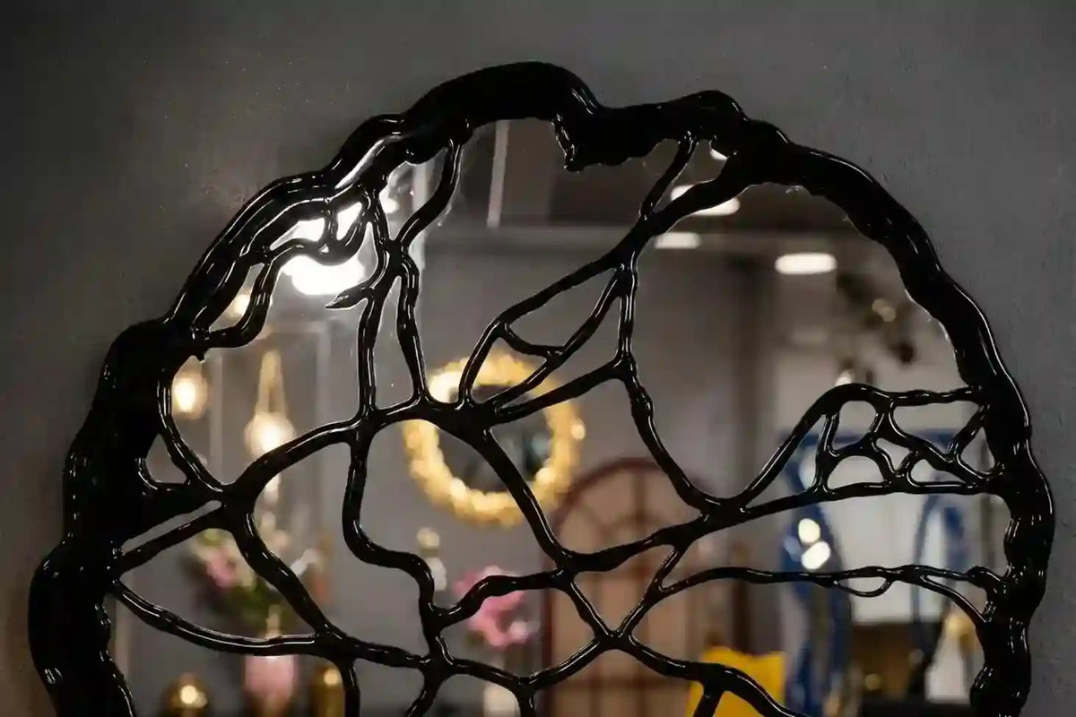 A black, organic-shaped decorative mirror with a glossy, raised branch-like pattern, reflecting a softly blurred interior background.