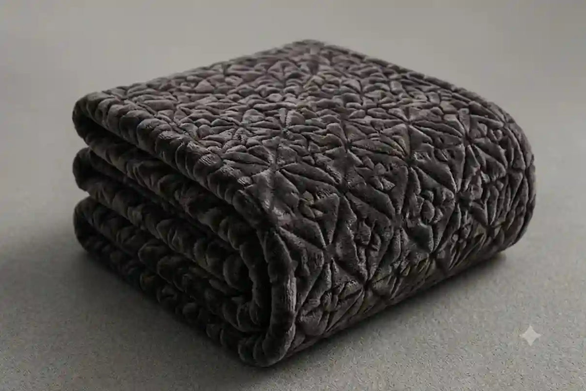 A folded dark gray quilted blanket with a textured geometric pattern, shown on a neutral gray background.