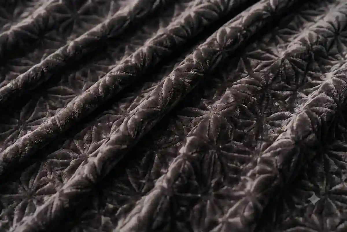 Close-up of a dark brown quilted fabric with a repeating floral starburst pattern and visible stitched texture.