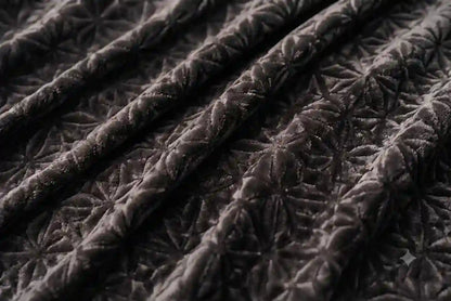 Close-up of a dark brown quilted fabric with a repeating floral starburst pattern and visible stitched texture.