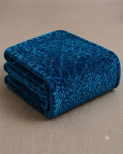 A folded teal blue velvet throw blanket with a subtle textured pattern, displayed on a neutral beige fabric background.