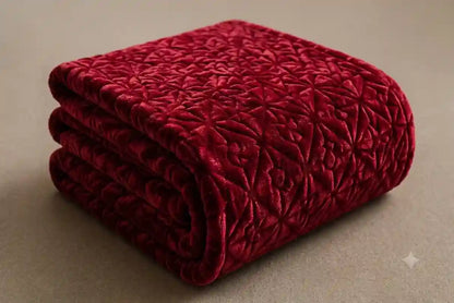 A folded deep red velvet throw blanket with an embossed geometric star pattern, set against a neutral beige background.