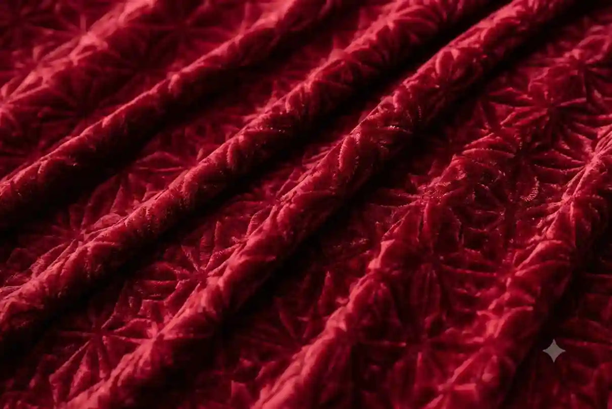 A close-up of deep red velvet fabric with a textured, embossed floral or geometric star pattern, draped in soft folds.