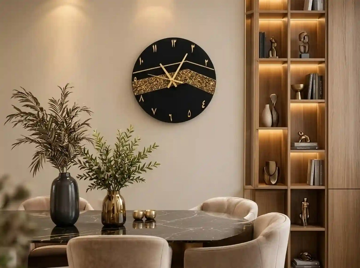 A round black wall clock with gold Roman numerals and a glittery gold wave design across the center, mounted on a beige wall in a modern dining room setting.