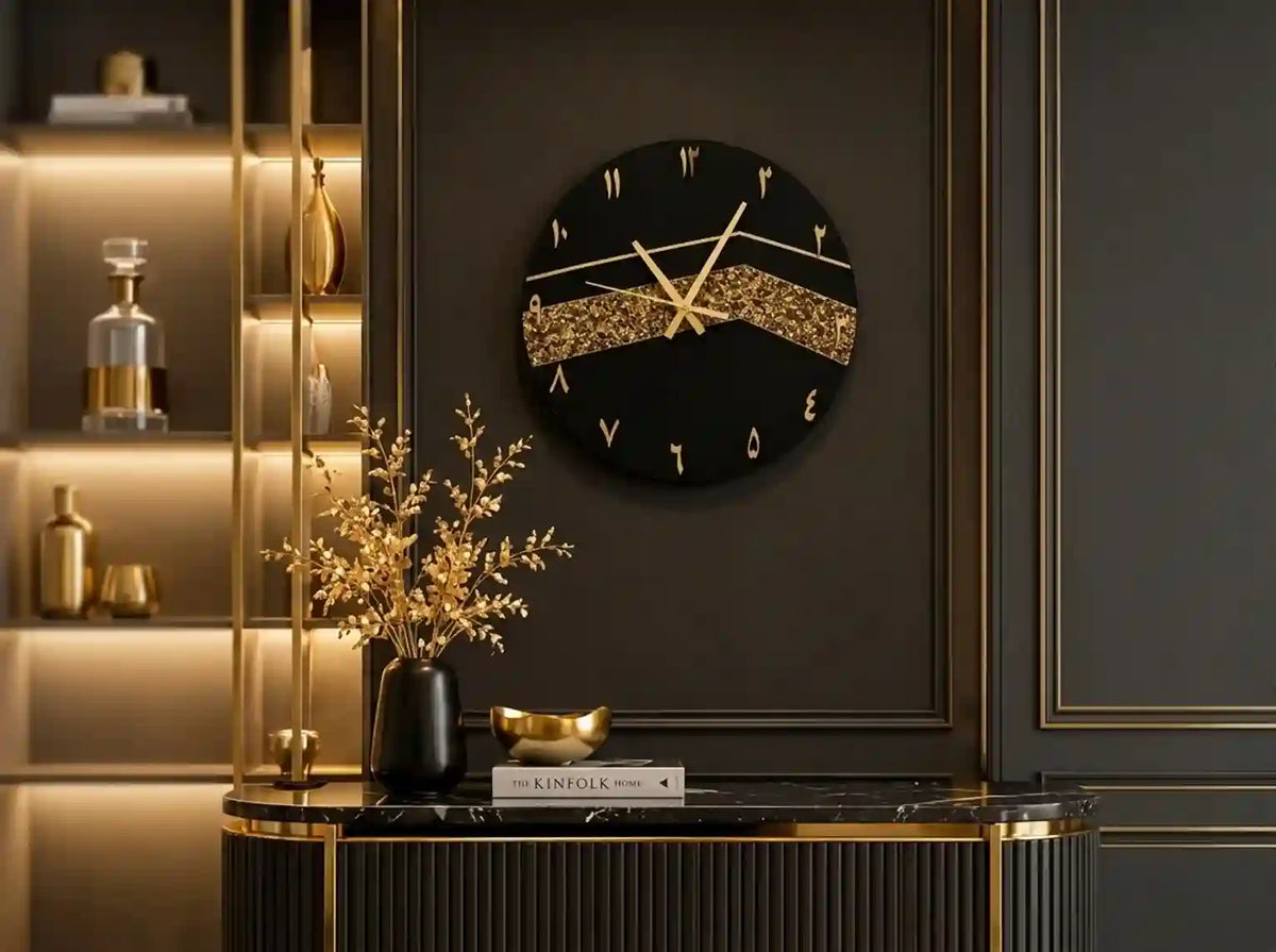 A round black wall clock with gold Roman numerals and a glittery gold center band, mounted on a dark paneled wall above a console table with decorative gold accents.