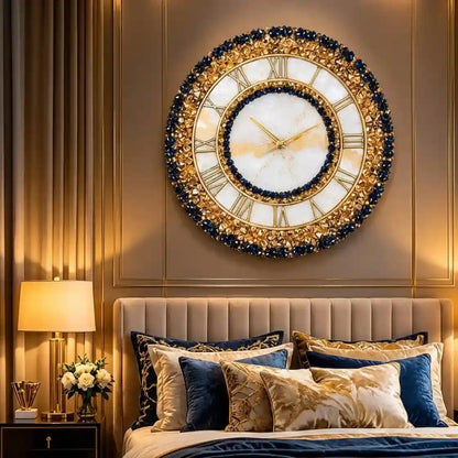 An ornate round wall clock with a gold and navy blue beaded frame, Roman numerals, and a white marble center, mounted on a gold-paneled bedroom wall above a bed with blue and gold pillows.
