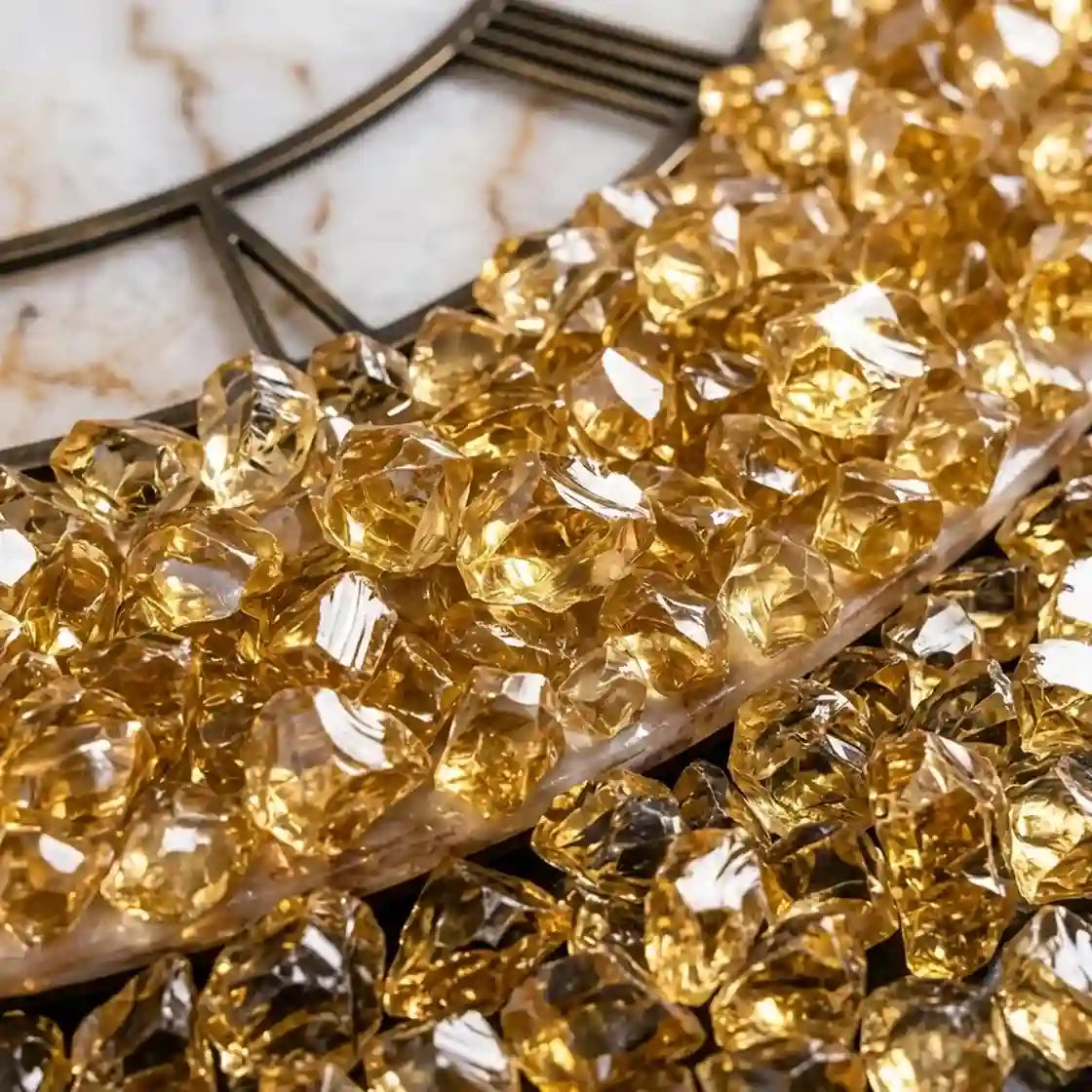Faceted clear crystal-like decorative pieces with warm golden reflections, arranged on a marble surface with a dark metal tray visible in the background.