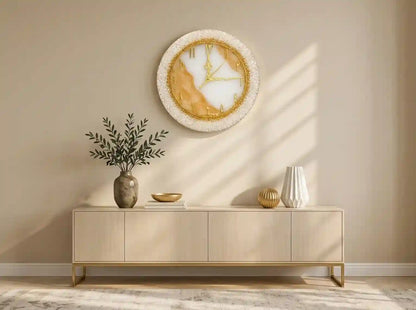 A modern sideboard console table in a warm beige wood finish with gold legs, styled in a minimalist room with a round gold and white marble wall clock, a vase with greenery, and decorative vases.