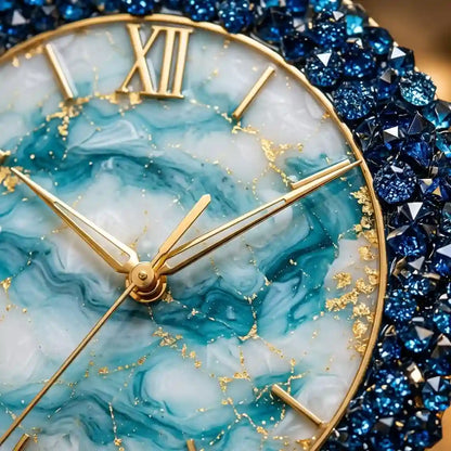 Close-up of a round wall clock with a marbled aqua and white dial, gold Roman numerals and hands, and a sparkling deep blue crystal bezel.