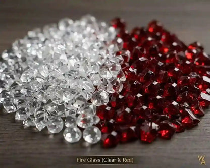 A pile of faceted fire glass rhinestones split into two distinct colors: clear, transparent stones on the left and deep red, transparent-red stones on the right, displayed on a dark wooden surface.