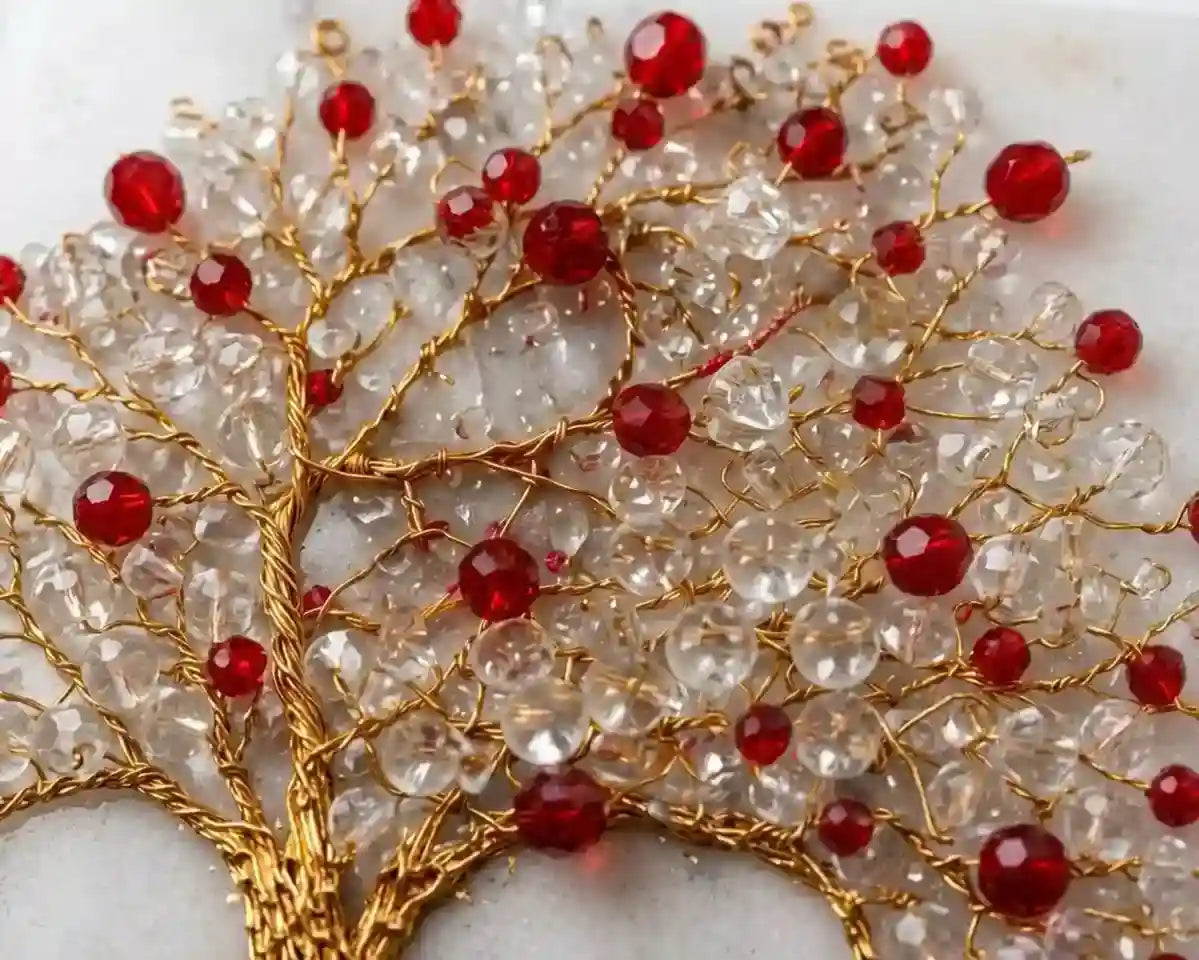 A close-up of a decorative tree design made of clear faceted beads on a gold wire frame, accented with multiple red faceted beads, set against a light neutral background.