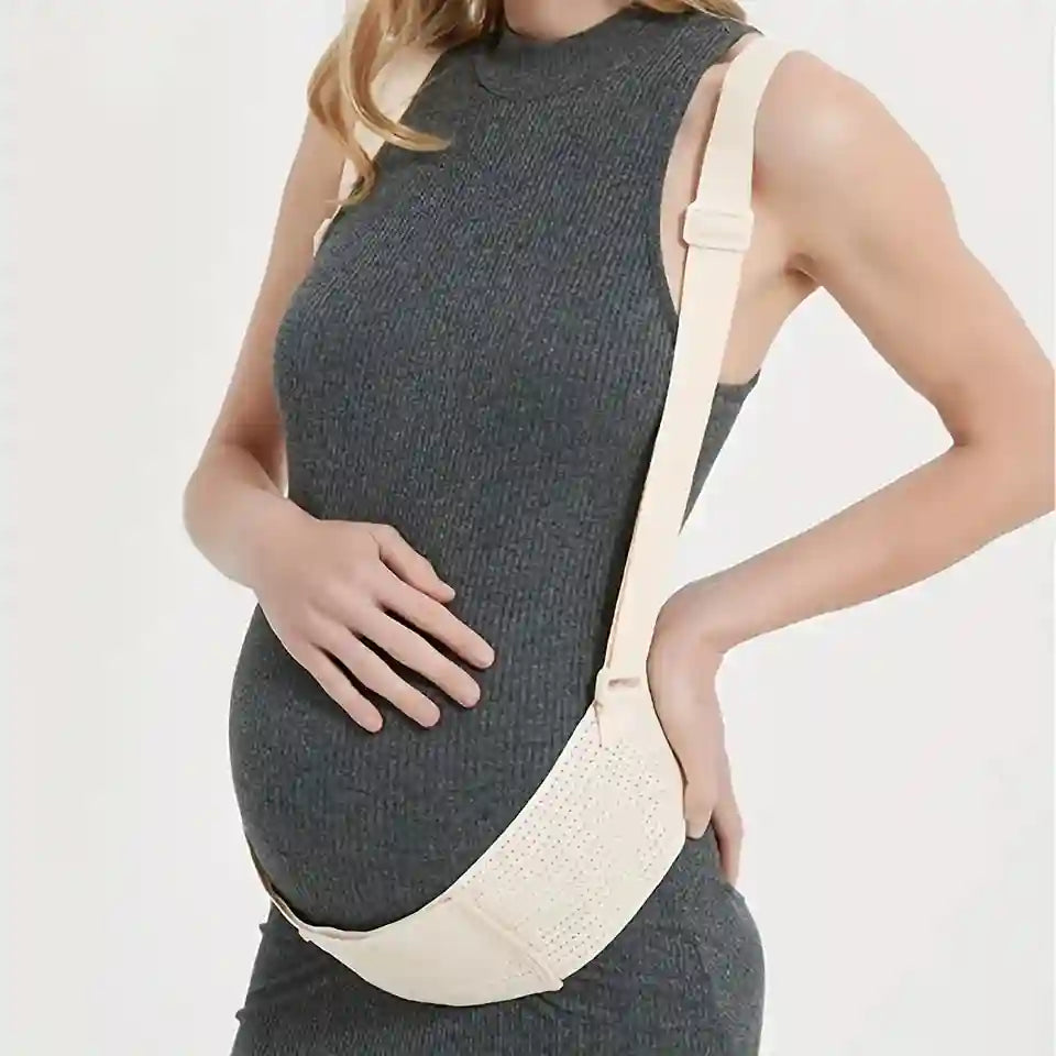 A pregnant model wearing a dark gray ribbed knit maternity dress and a cream-colored underbust belly support belt with an adjustable shoulder strap, shown against a plain white background.
