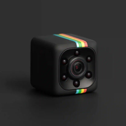 A black cube-shaped mini camera with a colorful rainbow stripe on the top and bottom edges, featuring a central lens surrounded by six dark sensors, set against a dark gray background.