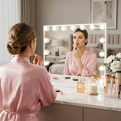 Woman applying makeup in front of a vanity mirror with lights, in a bedroom setting.