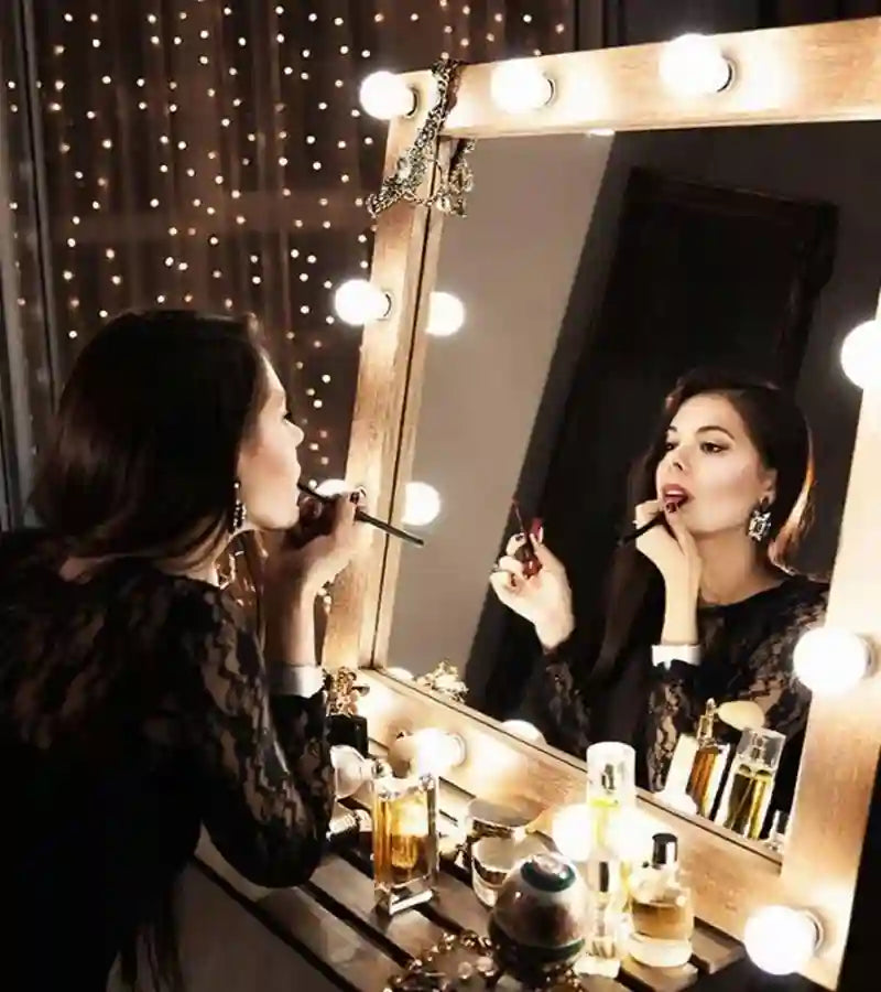 Woman applying makeup in front of a vanity mirror with lights.