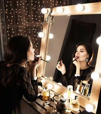 Woman applying makeup in front of a vanity mirror with lights.