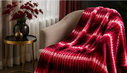 A plush throw blanket with a red and pink tie-dye pattern draped over a beige armchair in a cozy living room setting.