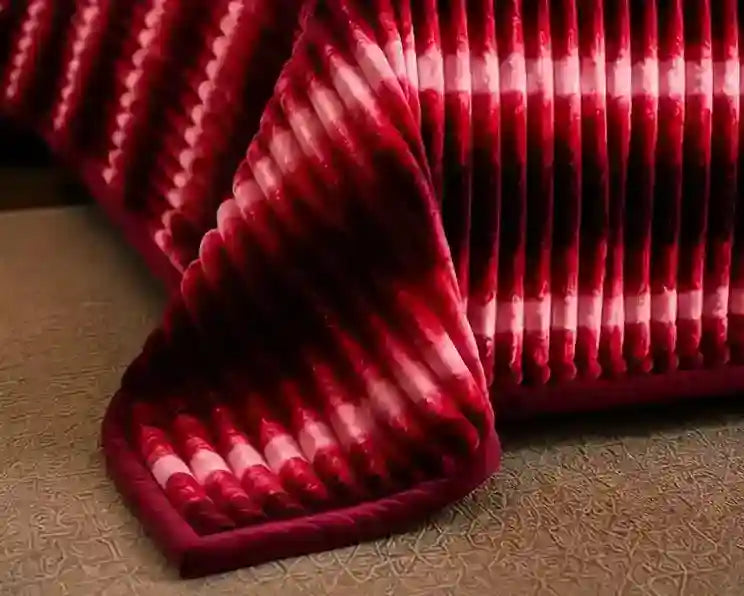A close-up of a pleated fabric accessory, likely a pillowcase or decorative pillow cover, featuring a deep red and white tie-dye pattern with a thick red border, resting on a textured beige surface.