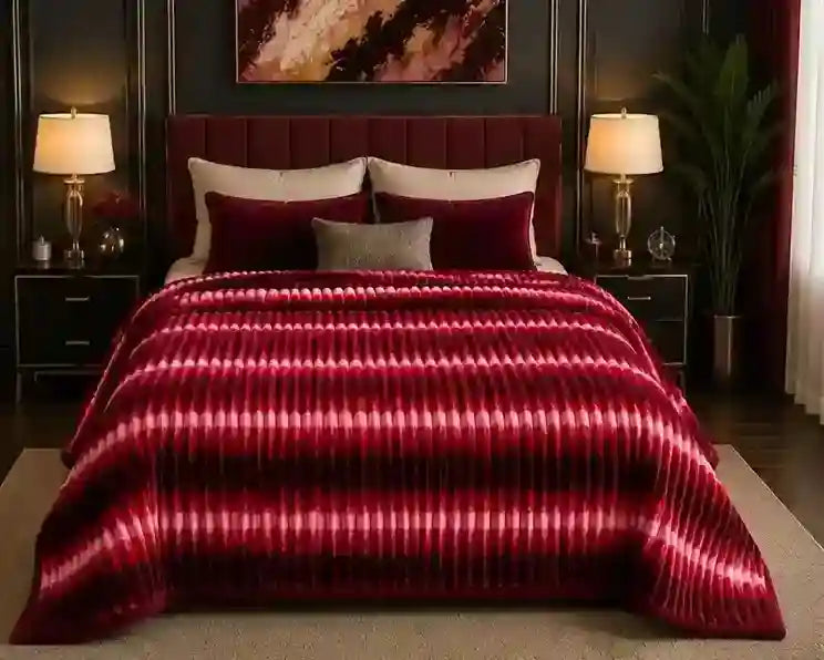 A bed dressed in a plush burgundy and magenta striped comforter set with matching pillows, styled in a dark, elegant bedroom with bedside lamps and a plant.