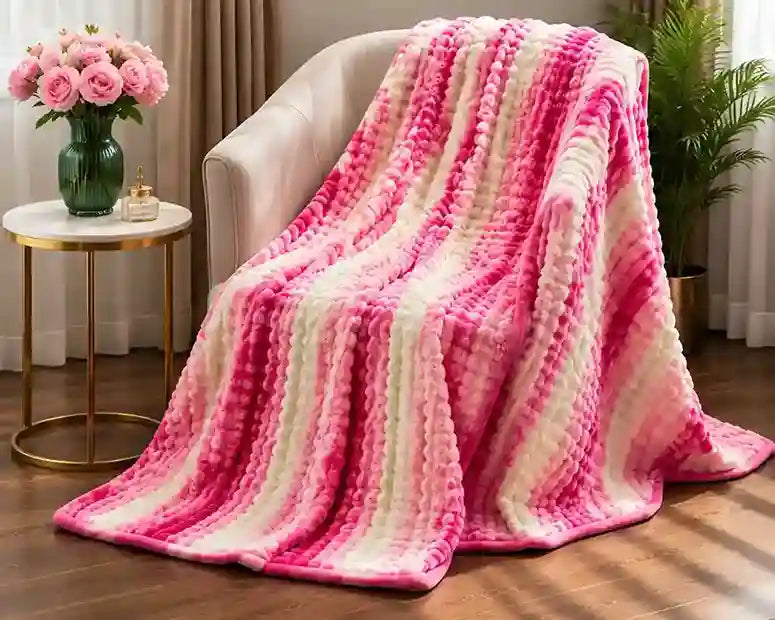 A plush, chunky knit throw blanket with vertical stripes of pink and cream draped over a beige armchair in a cozy living room setting.