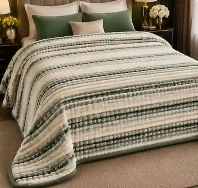 A striped quilted blanket in cream, beige, and sage green tones, styled on a bed with matching pillows in a bedroom setting.