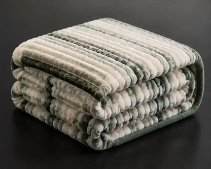 A folded plush striped blanket with alternating cream and sage green ribbed sections, displayed on a dark reflective surface.