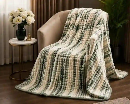 A textured striped throw blanket draped over a beige armchair in a cozy living room setting, featuring alternating vertical stripes of sage green, cream, and light beige.