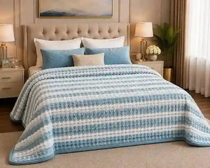 A cozy bedroom scene featuring a bed made with a textured, striped blue and white blanket, blue pillows, and neutral beige bedding. The room is styled with matching bedside tables, lamps, a curtain, and a framed picture on the wall.