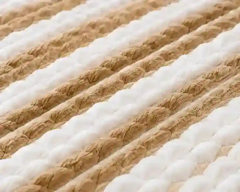 A close-up of a thick braided rug or mat with alternating diagonal stripes of white and natural tan jute.