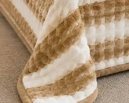 A close-up of a textured quilted blanket with alternating thick stripes of cream white and warm tan bouclé fabric, draped over the corner of a bed.
