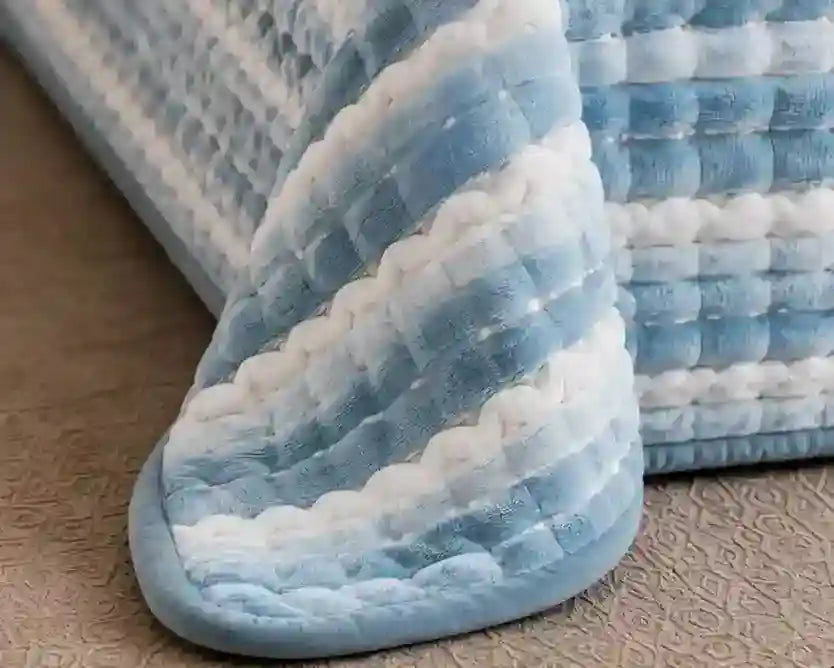 A close-up of a textured, quilted blanket or cushion in soft blue and white stripes, resting on a beige patterned floor.