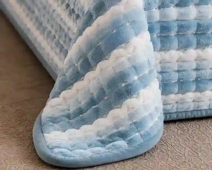A close-up of a textured, quilted blanket or cushion in soft blue and white stripes, resting on a beige patterned floor.