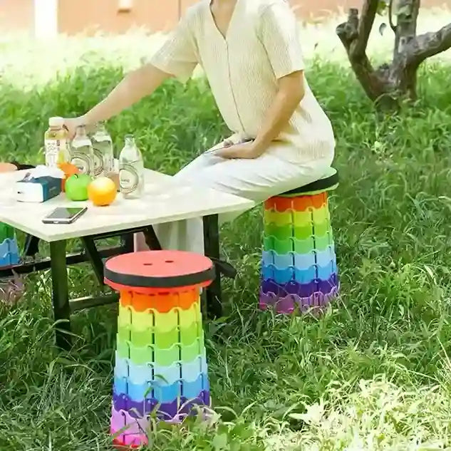 Person sitting on a colorful folding stool outdoors near a picnic table.