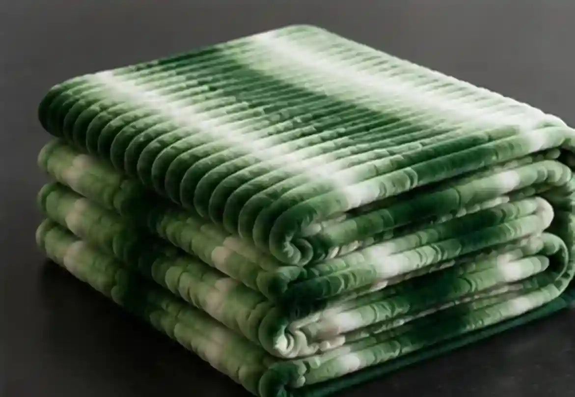 A stack of folded plush blankets in a green and white tie-dye pattern, set against a dark gray background.