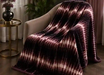 A plush throw blanket with a vertical ribbed texture and a tie-dye pattern in dark purple, burgundy, and light pink, draped over a beige armchair in a living room setting.