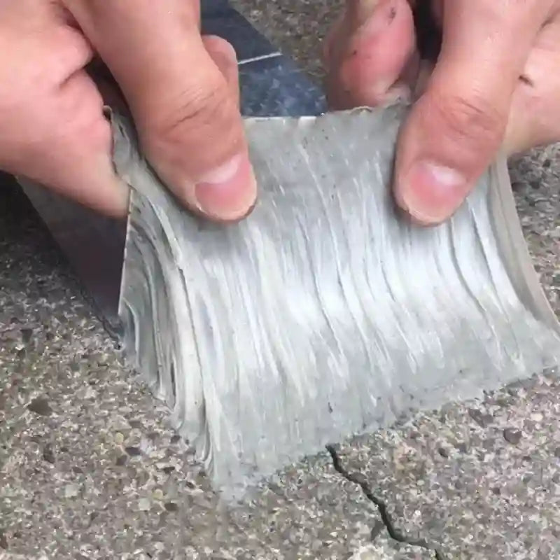A close-up of a person's hands bending a flexible, textured gray strip of material over rough concrete ground.
