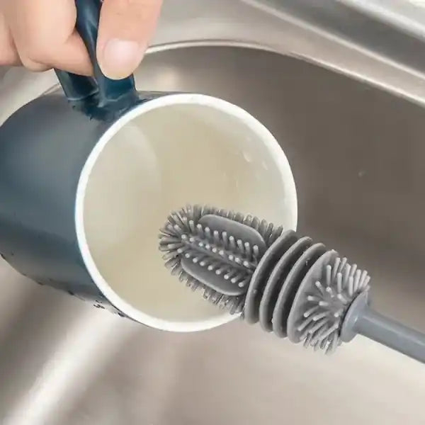 Gray bottle brush cleaning a white cup in a sink