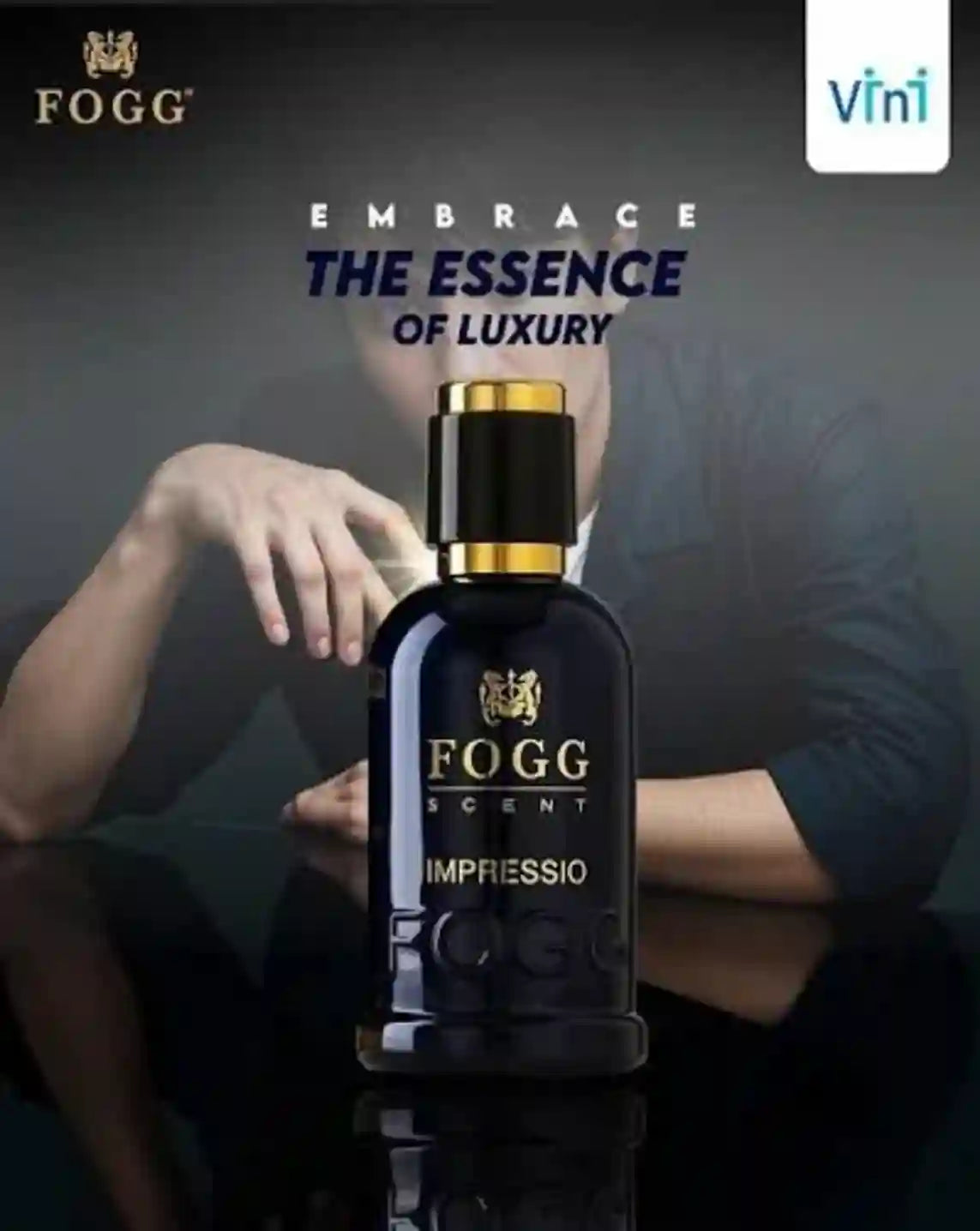 Fogg Scents Impressio perfume bottle in a dark navy blue glass with gold lettering and a gold cap, set against a dark background with a blurred man in a suit behind it. Fogg branding is visible, along with a Vini logo in the top right corner.