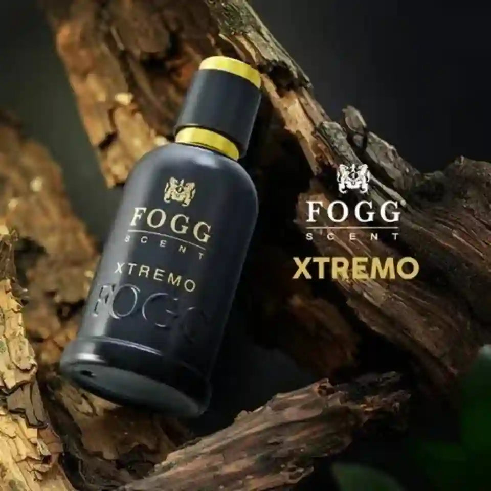 A dark frosted glass bottle of Fogg Scent Xtremo perfume with a black cap and gold accents, resting on textured wood logs. The brand logo and name 'Fogg Scent Xtremo' are displayed on the right side of the image.