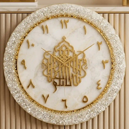 An ornate round wall clock with a white marble face, gold Arabic numerals and hands, and a crystal-encrusted gold outer rim, mounted on a beige ribbed wall.