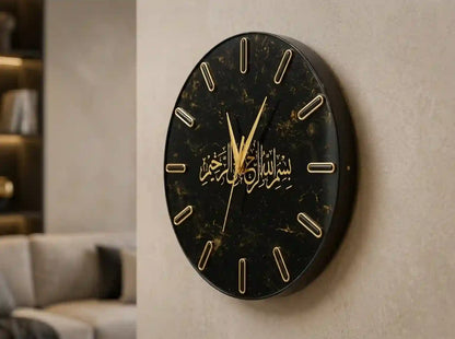 A round black marble-patterned wall clock with gold Arabic calligraphy and gold hour markers, mounted on a textured beige wall in a modern interior setting.
